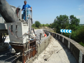 Ouvrier en train de mettre en place le long d'une route une bordure coulée grâce à une machine